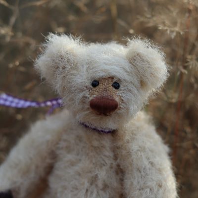 Miniatur Teddy Waldzwerg aus Alpaka in hell-beige mit dunkelbrauner Nase vor Gräsern
