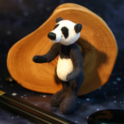 Waldzwerge Miniatur Panda Teddy aus kurzem upholstery velvet Stoff steht vor einer Holzschiebe vor schwarzem Hintergrund