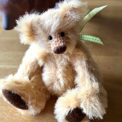 beigefarbene Waldzwerge Miniatur Teddy Dame mit brauner Nase und Sohlen sitzt auf einem Holztisch