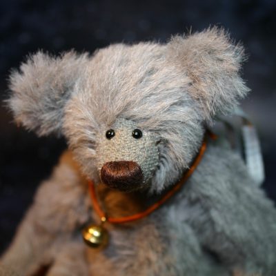 Nahaufnahme des Kopfes eines grauen Alpaka Teddys mit brauner Nase vor einem dunklen Hintergrund